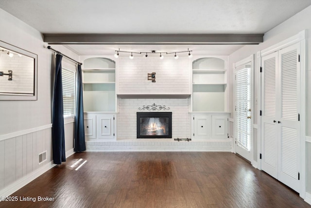unfurnished living room with wood finished floors, a brick fireplace, built in features, healthy amount of natural light, and beam ceiling