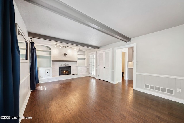 unfurnished living room with wood finished floors, a fireplace, beam ceiling, built in features, and a wainscoted wall