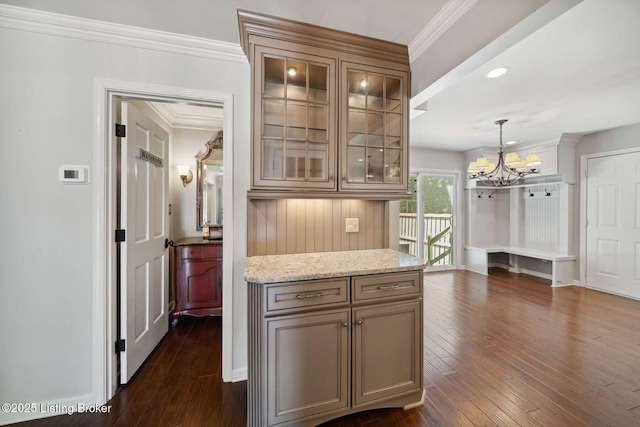 kitchen with a chandelier, dark wood finished floors, glass insert cabinets, ornamental molding, and light stone countertops