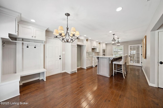 kitchen with a chandelier, recessed lighting, white cabinetry, a kitchen bar, and baseboards