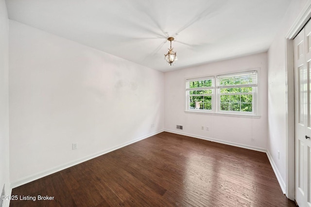 empty room with dark wood finished floors, baseboards, and a chandelier