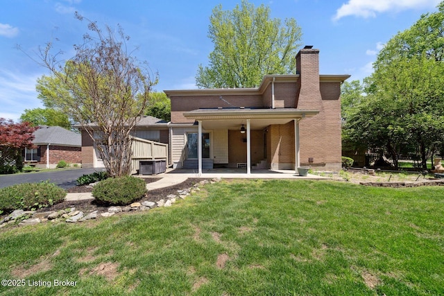 rear view of property featuring a chimney, a patio, a yard, ceiling fan, and brick siding