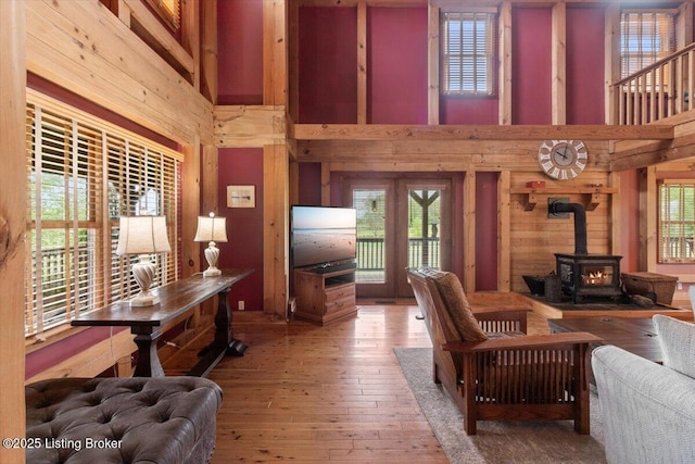 living room with a high ceiling, wooden walls, a wood stove, wood-type flooring, and plenty of natural light