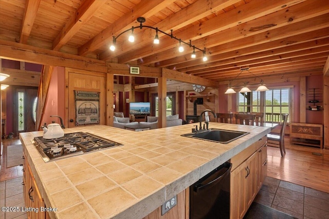 kitchen with tile countertops, stainless steel gas cooktop, a sink, beamed ceiling, and black dishwasher