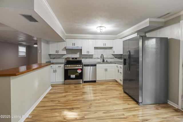 kitchen with appliances with stainless steel finishes, a sink, dark countertops, light wood finished floors, and ornamental molding