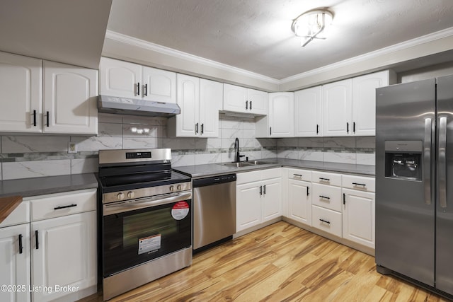 kitchen with appliances with stainless steel finishes, a sink, under cabinet range hood, crown molding, and dark countertops