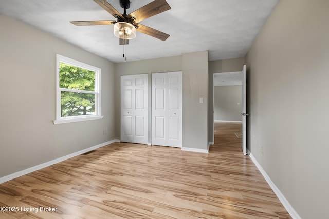 unfurnished bedroom featuring multiple closets, light wood-style floors, and baseboards
