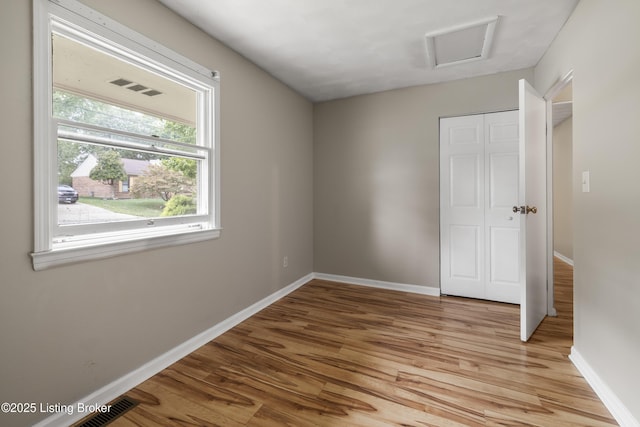 unfurnished bedroom featuring multiple windows, light wood-style flooring, baseboards, and attic access
