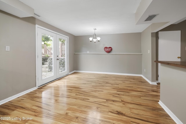 unfurnished dining area with wood finished floors, french doors, baseboards, and a chandelier