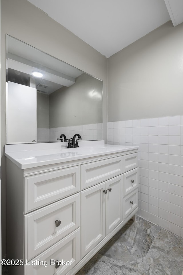 bathroom featuring tile walls, vanity, marble look tiles, and wainscoting