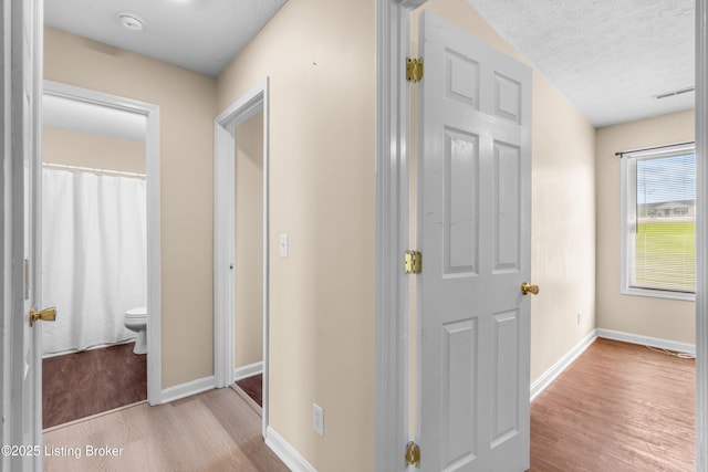 hall with wood finished floors, baseboards, and a textured ceiling