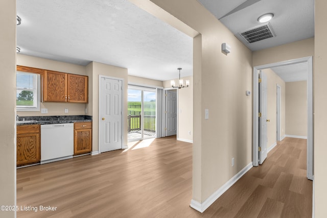 kitchen featuring white dishwasher, brown cabinets, a chandelier, dark countertops, and light wood-style floors