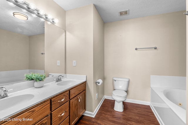 bathroom featuring a bath, wood finished floors, toilet, baseboards, and double vanity