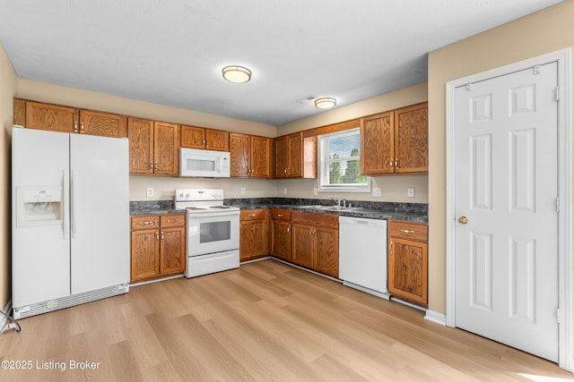 kitchen featuring white appliances, dark countertops, brown cabinets, and light wood-style flooring