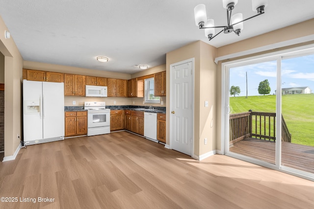 kitchen with white appliances, dark countertops, light wood-style floors, brown cabinetry, and a chandelier
