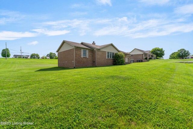 view of side of property featuring brick siding, a lawn, and a chimney