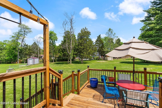 wooden terrace with a storage unit, an outbuilding, a lawn, and view of wooded area