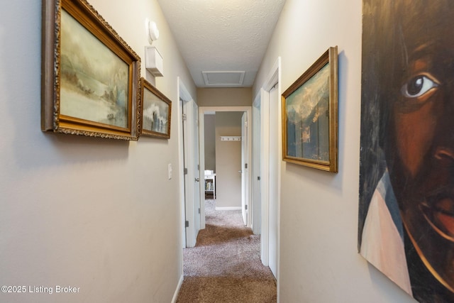 corridor featuring carpet, attic access, a textured ceiling, and baseboards