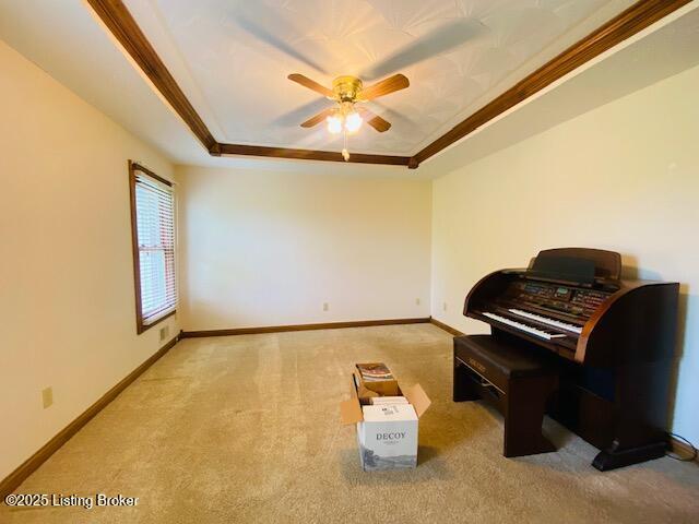living area with a raised ceiling, a ceiling fan, carpet, baseboards, and crown molding