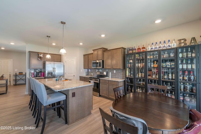 11905 Parkside Vista Ln, Louisville, KY 40229 - kitchen featuring appliances with stainless steel finishes, light wood finished floors, decorative backsplash, a breakfast bar area, and an island with sink