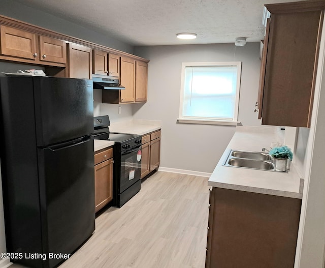 kitchen with black appliances, under cabinet range hood, light wood-style flooring, light countertops, and a sink