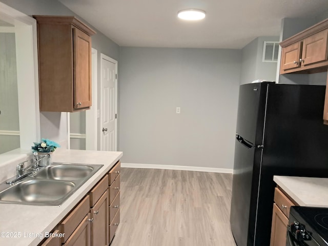 kitchen with a sink, light wood-style flooring, light countertops, black appliances, and baseboards