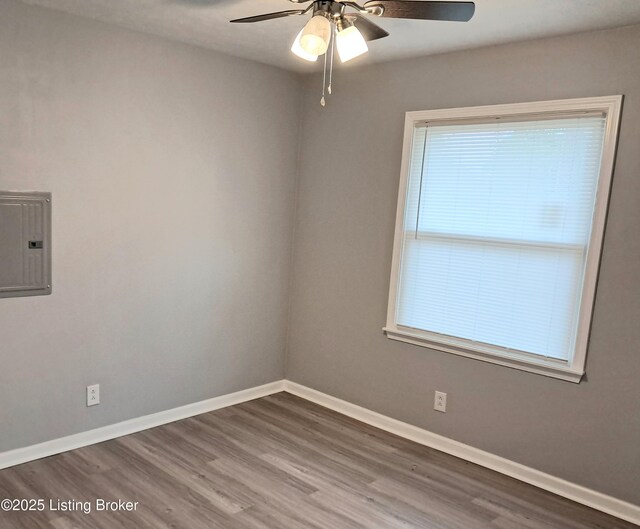 empty room with electric panel, wood finished floors, a ceiling fan, and baseboards