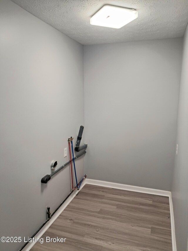 clothes washing area with wood finished floors, hookup for a washing machine, a textured ceiling, and baseboards