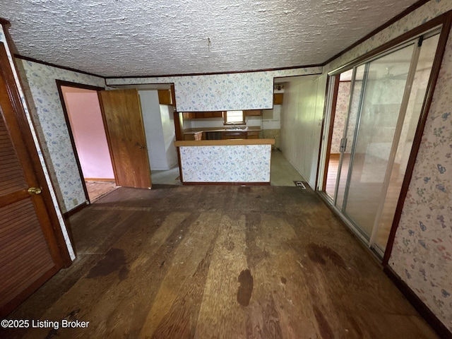 unfurnished living room with wallpapered walls, dark wood-type flooring, a textured ceiling, and baseboards