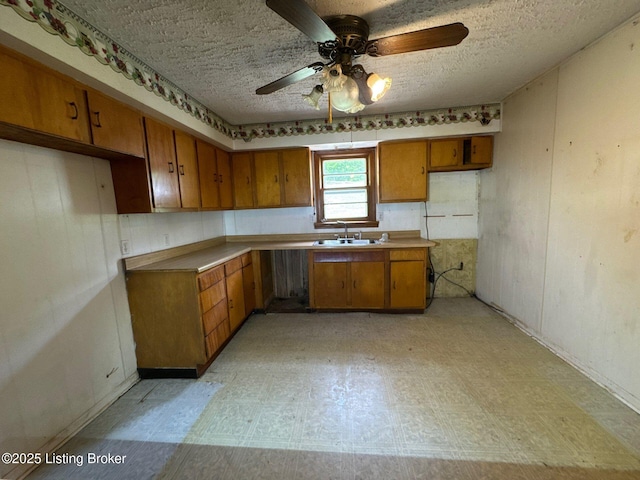 kitchen with brown cabinets, a sink, ceiling fan, a textured ceiling, and light floors
