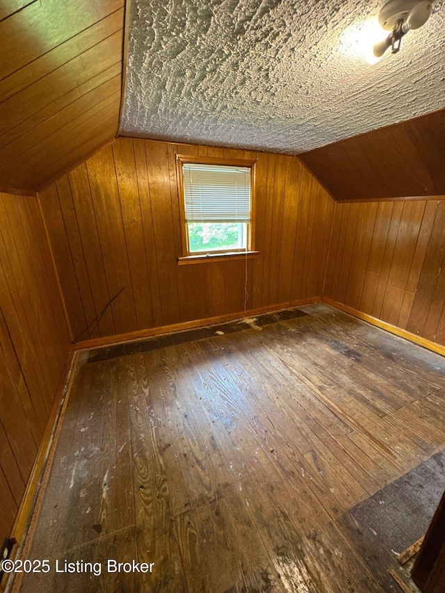 additional living space featuring hardwood / wood-style floors, lofted ceiling, and wood walls