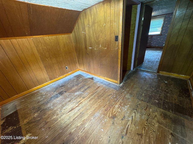 additional living space featuring wood-type flooring, lofted ceiling, wood walls, and baseboards