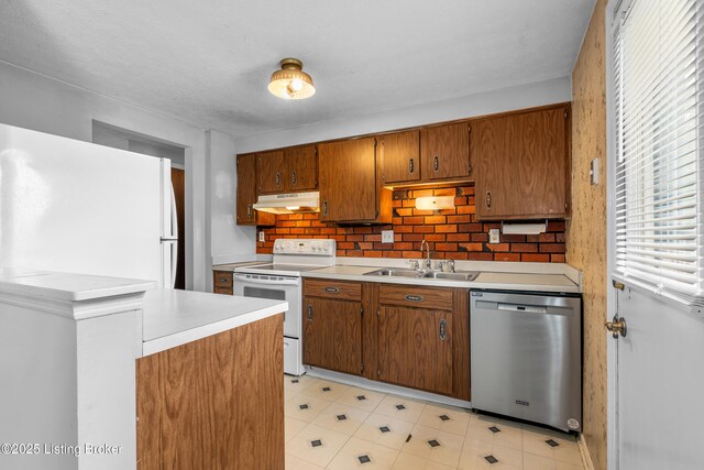 kitchen featuring white appliances, a sink, under cabinet range hood, light countertops, and brown cabinetry