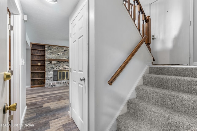 staircase featuring wood finished floors, a brick fireplace, built in shelves, and baseboards