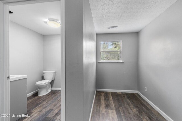 bathroom with toilet, wood finished floors, vanity, baseboards, and a textured ceiling