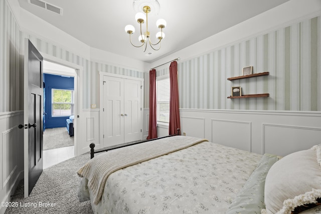 carpeted bedroom with a chandelier, a wainscoted wall, a decorative wall, a closet, and wallpapered walls