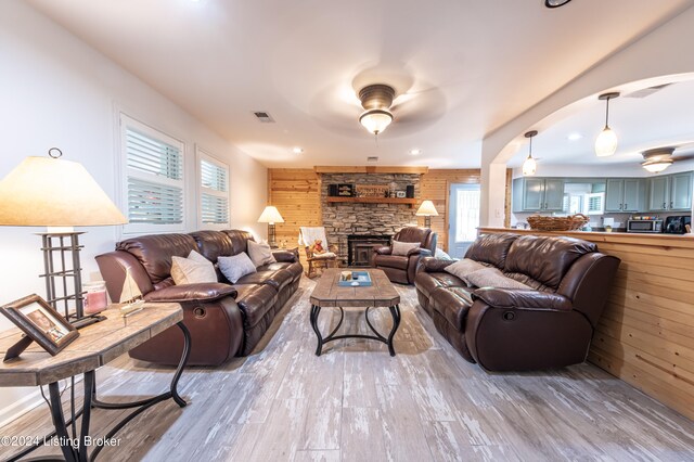 656 Hinton Hills Loop, Hardinsburg, KY 40143 - living area featuring light wood-type flooring, wooden walls, ceiling fan, arched walkways, and a stone fireplace