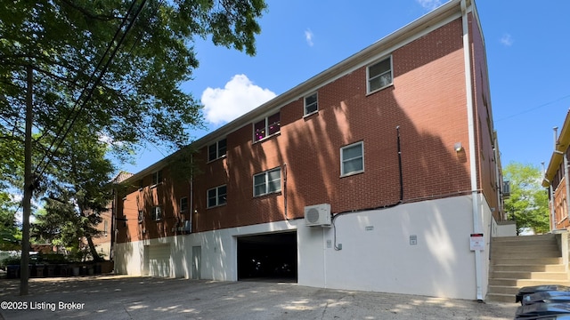 rear view of property featuring a garage, stairway, a cooling unit, and driveway