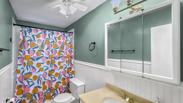 full bath with wainscoting, a decorative wall, a ceiling fan, toilet, and a shower with curtain