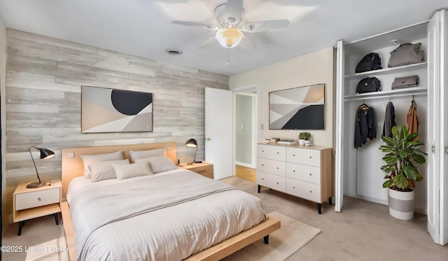 bedroom featuring light colored carpet, a ceiling fan, an accent wall, and a closet