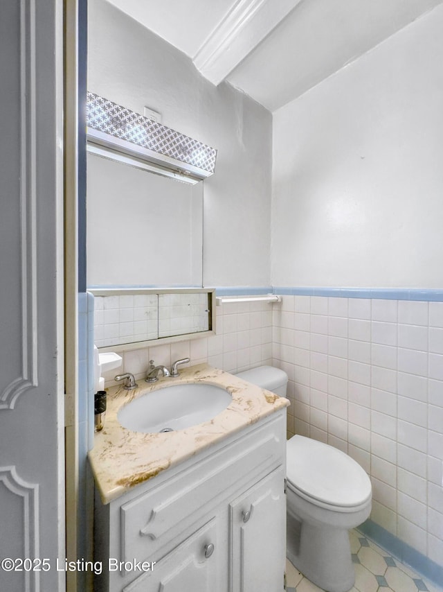 bathroom featuring toilet, vanity, tile walls, tile patterned floors, and a wainscoted wall