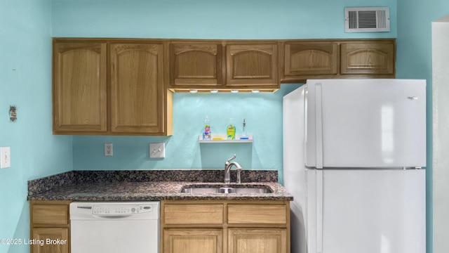 kitchen featuring white appliances, a sink, and dark stone countertops