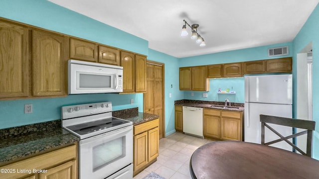 kitchen with white appliances, a sink, light tile patterned floors, dark stone countertops, and brown cabinetry