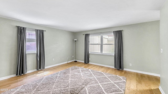unfurnished room with wood finished floors, healthy amount of natural light, and baseboards