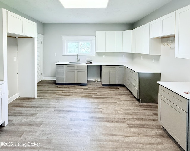 713 E Hill St, Louisville, KY 40217 - kitchen featuring a sink, light wood-type flooring, a skylight, and white cabinets