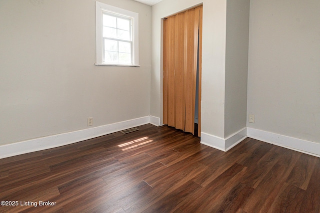 unfurnished bedroom featuring baseboards, dark wood-type flooring, and a closet
