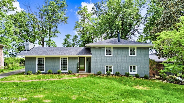 tri-level home featuring a front lawn, brick siding, a chimney, and roof with shingles