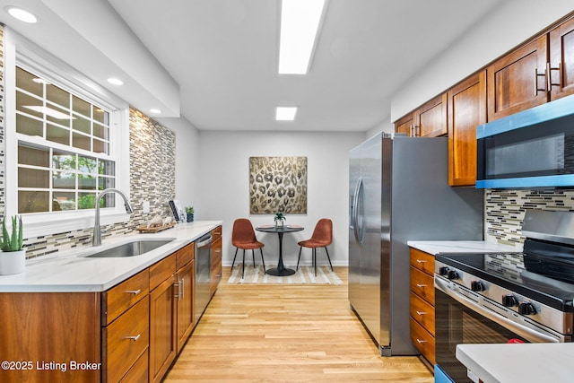 kitchen featuring appliances with stainless steel finishes, a sink, backsplash, light wood-type flooring, and recessed lighting