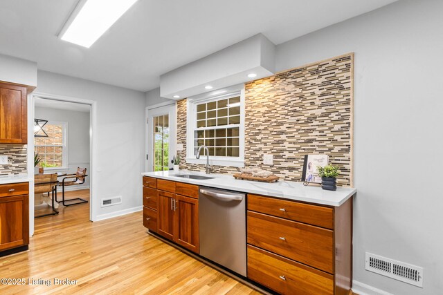 kitchen featuring a sink, dishwasher, tasteful backsplash, light wood finished floors, and light countertops
