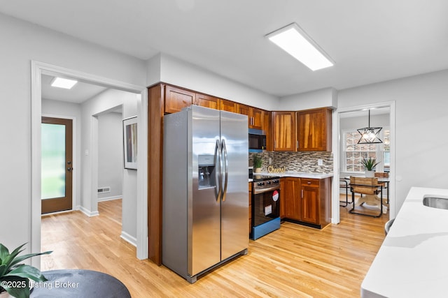 kitchen featuring stainless steel appliances, light countertops, light wood-style floors, tasteful backsplash, and brown cabinets